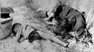 A black and white photo with adead child and a dead woman lying diagonally in a trench in the My Lai massacre